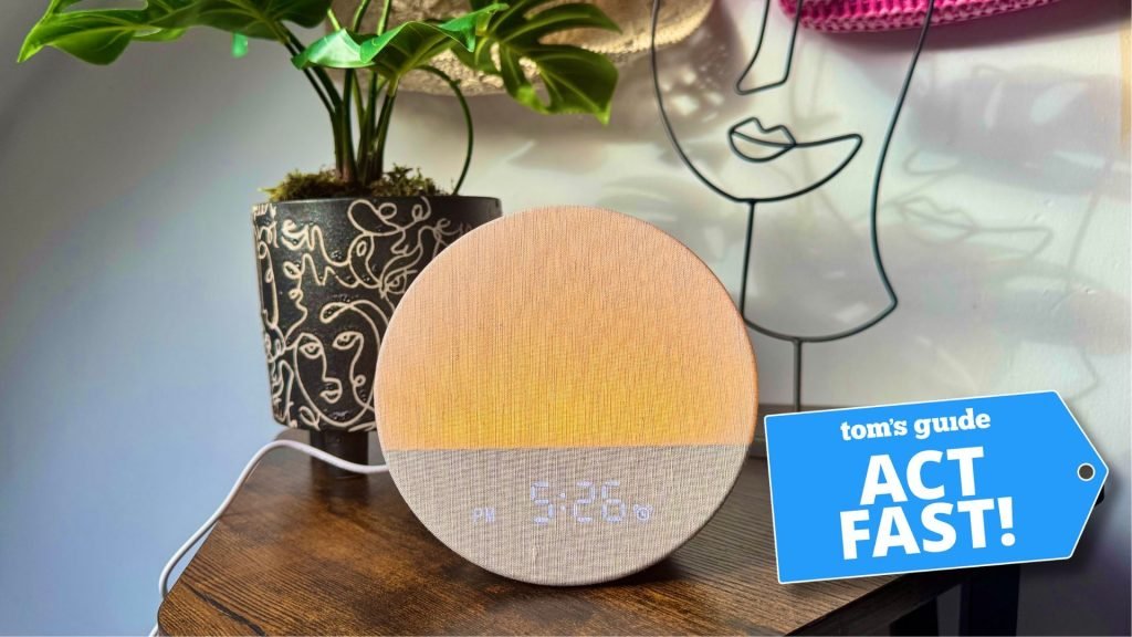 The Dreamegg sunrise alarm clock on wooden table next to plant in black and white patterned pot with Tom's Guide's 'act fast' logo