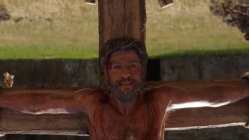 Saint Peter smiling gently while enduring crucifixion upside-down by the Romans, in a screenshot from docuseries "The Saints" season 2.