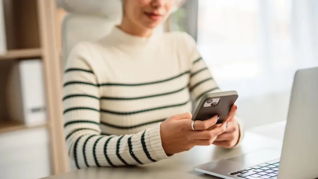 woman with headphones on holding a phone in front of laptop