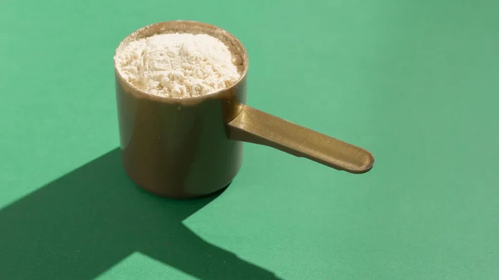 You Can Officially Stop Stressing About Your Protein Intake. An Expert Explains Why. A scoop of protein against a green background