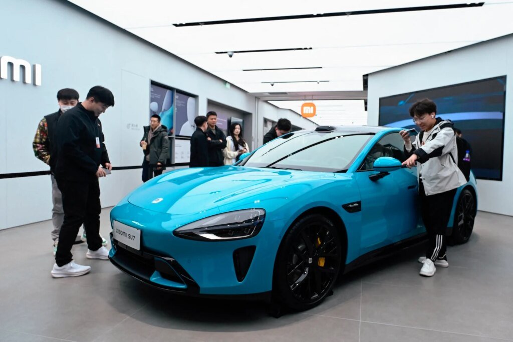 China Pumps Breaks on Plans to Mass Produce Self-Driving Cars Xiaomi's SU7 electric car displayed in a showroom, with individuals standing around it taking pictures.