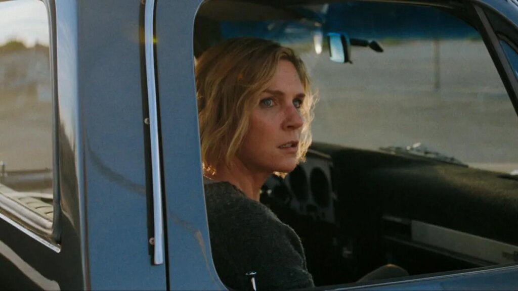 A still from the tv show Pluribus. A woman sits in a passenger seat of a pickup truck and looks out the window.