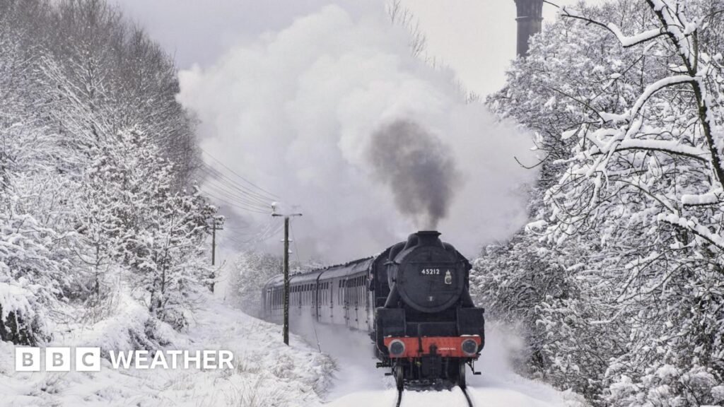 Steam train moving through snow-covered track lined with snow-covered trees