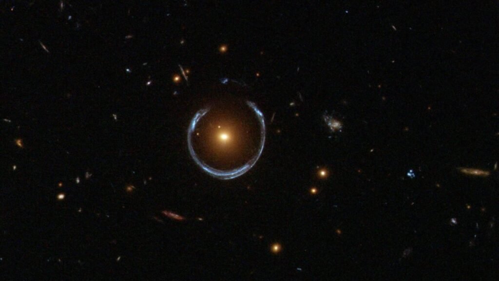 Image of a field of stars with a single bright object in the middle. The object is surrounded by a wispy, distorted ring.