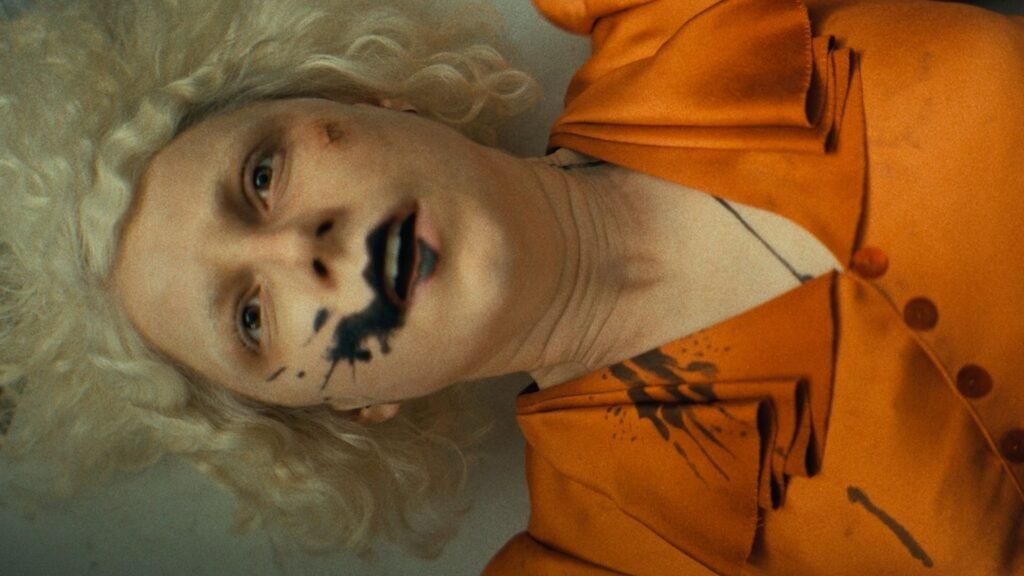 Jessie Buckley lays in a table with black dye around her mouth