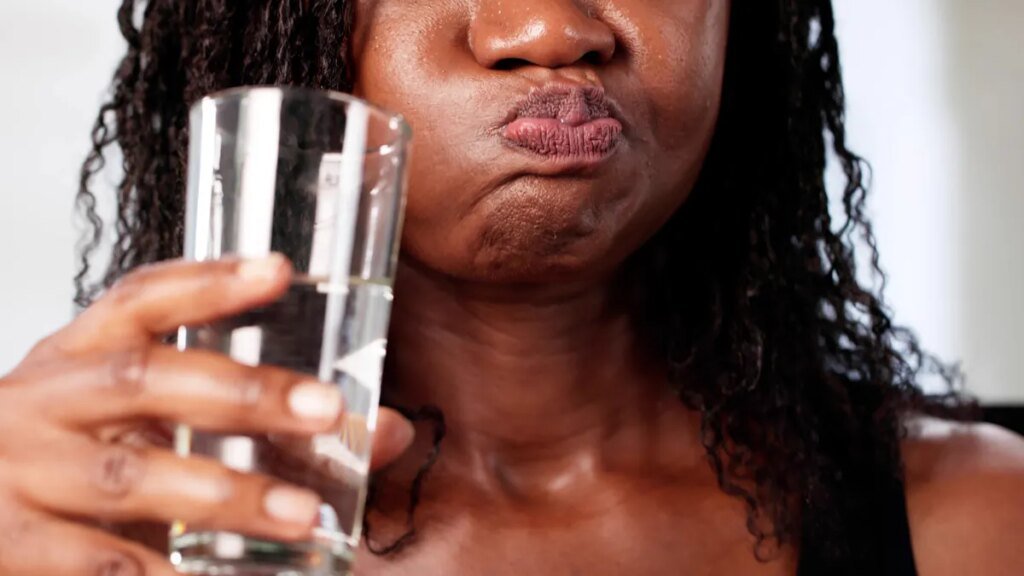 Stop Rinsing After Brushing Your Teeth. Here’s Why A person holding a glass is swishing their mouth with water.