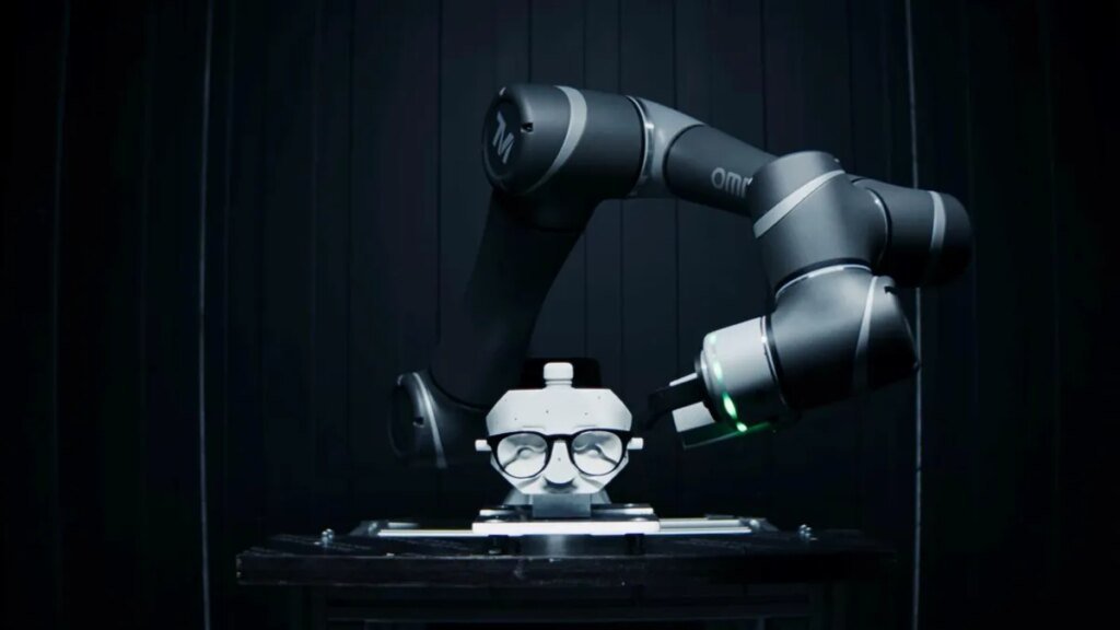 a robotic arm hovers over a pair of eyeglasses that are resting on a face sculpture.