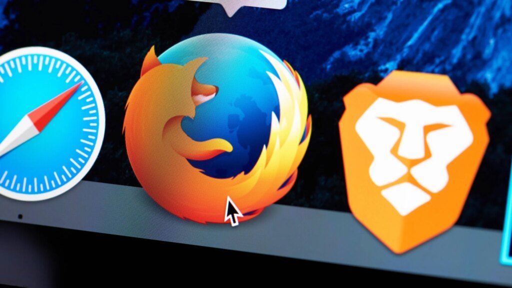 Mozilla Adding ‘Off’ Switch to AI in Firefox A mouse cursor hovering over the Firefox icon on a desktop, in between icons for Brave and Safari
