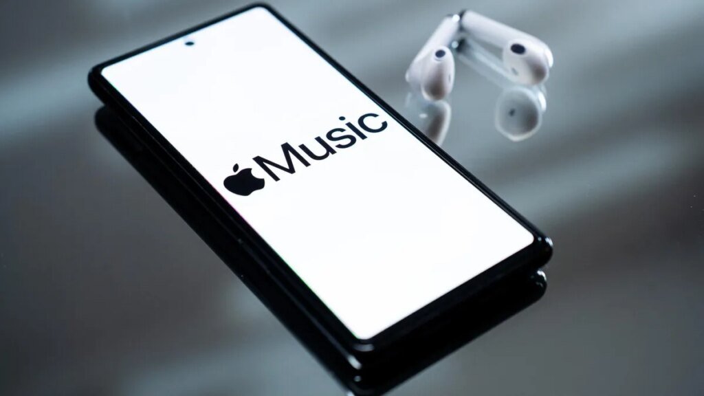 An image of a smart phone with the Apple Music logo in black text on a white background sitting next to a pair of white airpods.