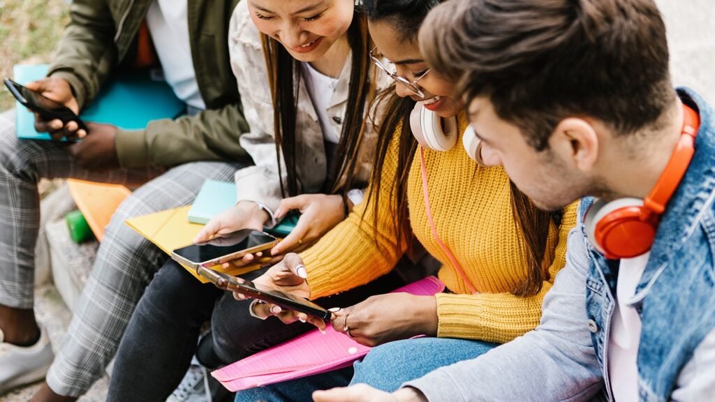 Young adults looking at smartphones on a bench or low wall